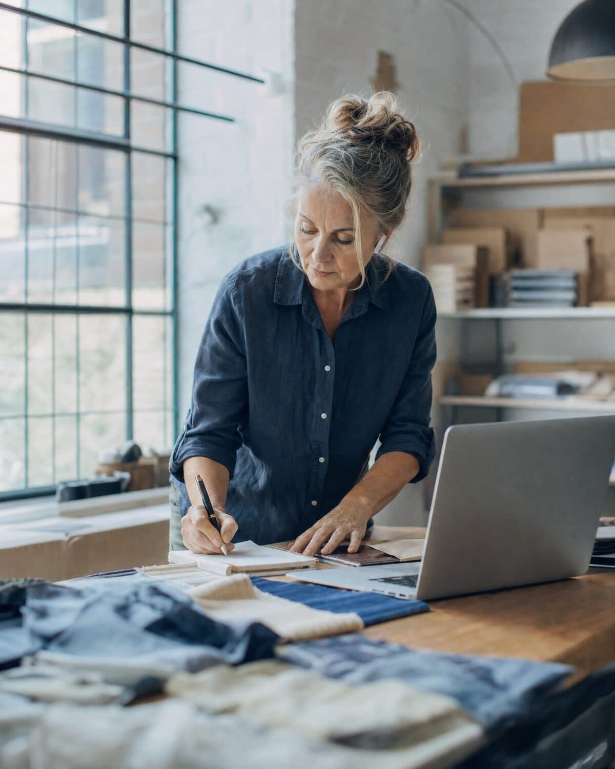 A workshop owner taking notes during a call to a supplier, laptop on the workbench